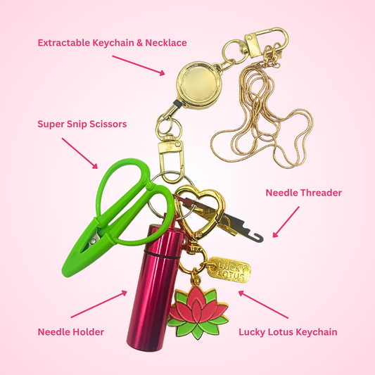 Retractable Needlepoint Tool Necklace featuring a gold-tone chain, retractable reel, Super Snip scissors, magnetic needle holder, needle threader, and Lucky Lotus enamel charm.