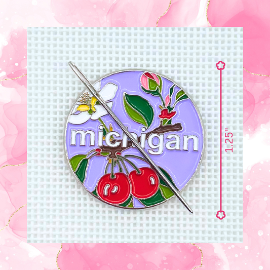 Michigan state needlepoint needle minder close up featuring cherries, apple blossom, greenery, and a needle on a purple background.