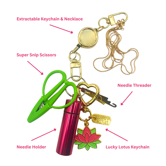 An extractable keychain and necklace set with attached accessories, shown on a white background with pink labeled callouts. The set includes a gold-tone retractable badge reel and chain, green super snip scissors, a metallic pink needle holder, a gold heart-shaped needle threader, a gold lucky lotus tag, and a red and green lucky lotus charm.