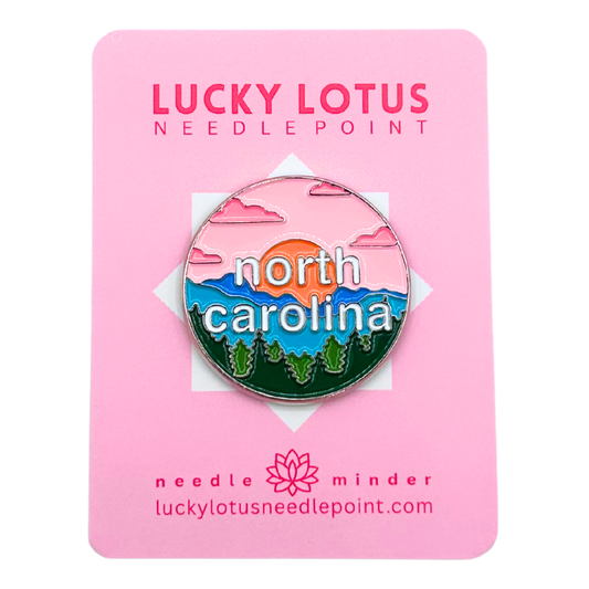 North Carolina needle minder featuring layered blue mountains, evergreen trees, a colorful sunset, and North Carolina lettering.