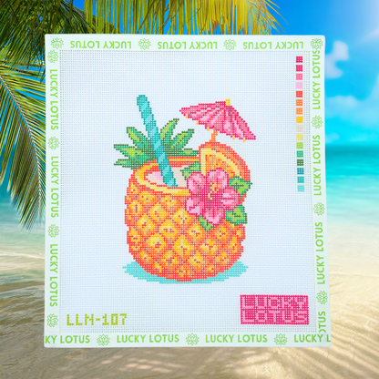 Lucky Lotus Needlepoint pineapple cocktail canvas displayed against a bright tropical beach background with palm trees and turquoise water.