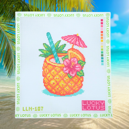 Lucky Lotus Needlepoint pineapple cocktail canvas displayed against a bright tropical beach background with palm trees and turquoise water.