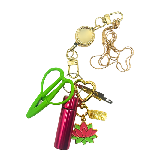 Retractable Needlepoint Tool Necklace featuring a gold-tone chain, retractable reel, Super Snip scissors, magnetic needle holder, needle threader, and Lucky Lotus enamel charm.
